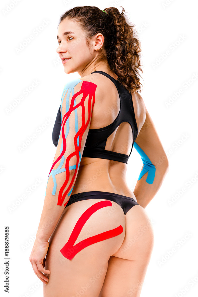 sexy female athlete with beautiful booty stands half sideways on white  background in black top and bikini.On body is pasted kinesiology tape.Colored  tapes for treatment of muscles,tendons in athletes foto de Stock