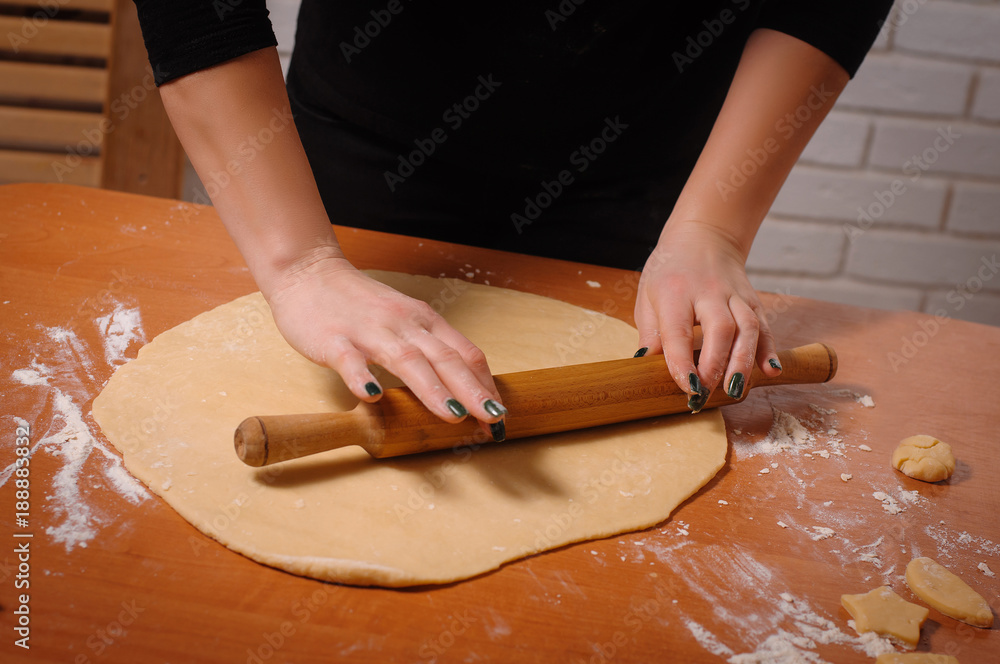 rolling dough for a cookie on the table. The female hands form the dough with a rolling pin