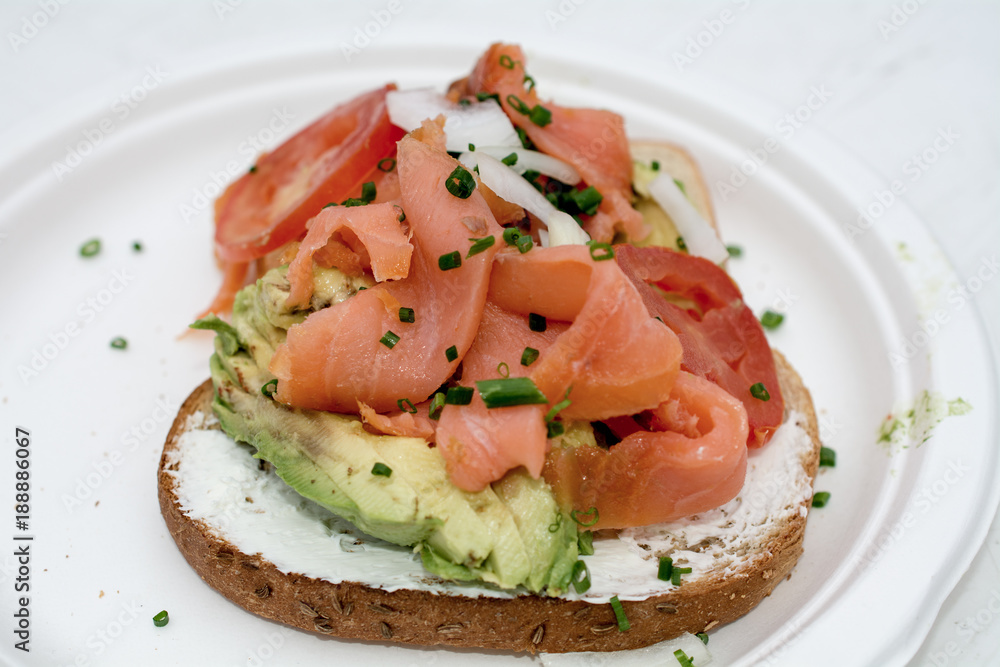 Avocado toast with smoked salmon on white plate and table outdoors Avocado toast with smoked salmon on white plate and table outdoors