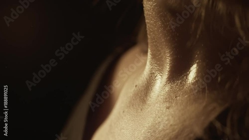 Close-up of a WOMAN applying perfume on her neck. Dim light emphasizes skin texture and sensuality.