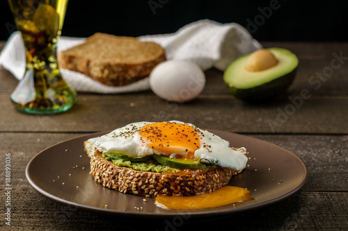 sandwich with avocado and a fried egg on a brown plate on a rustic wood and table bread on white kitchen towel.