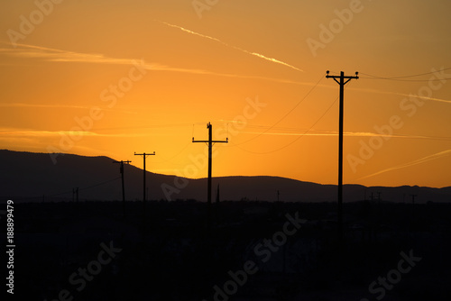 A row of telephone poles provide contrast in front of an orange sunset over a mountain range. © KilmerMedia