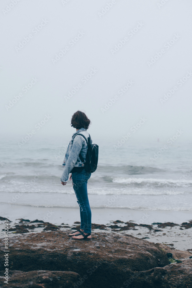 Woman with backpack looking at sea waves