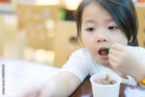 Little asian girl boring when she eating chocolate ice cream cup alone.