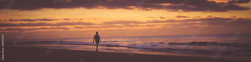 Some person is walking along the beach at sunrise. Banner photography format.