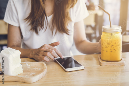 Young woman using smart phone and eating cake in cafe