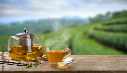 Cup of hot tea and glass jugs or jars and tea leaf on the wooden table and the tea plantations background