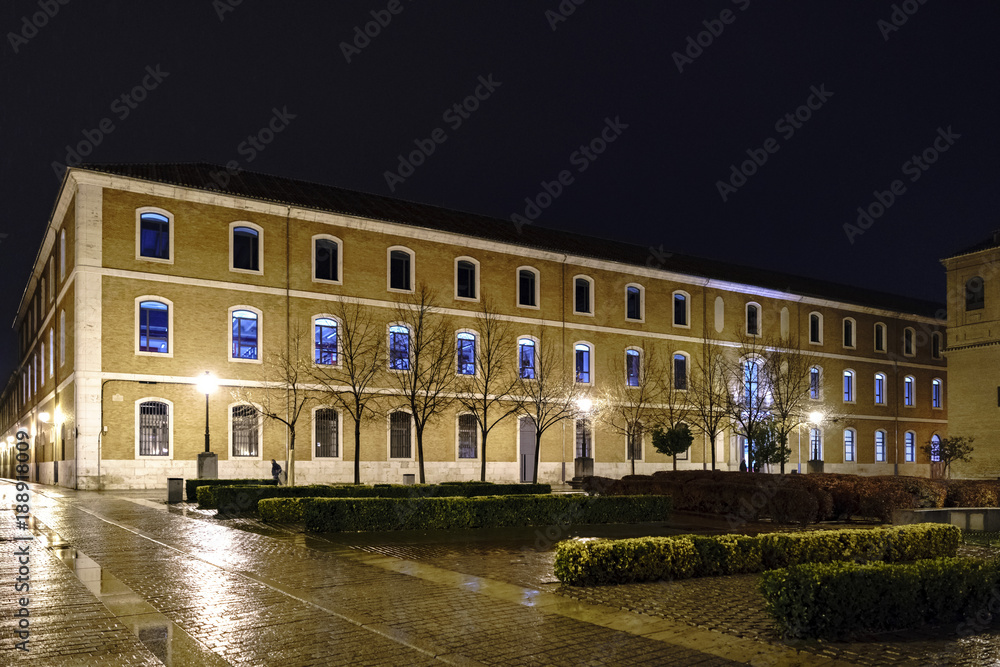 Old brick facade of the library of the University of Alcala de Henares, Spain on a cold and rainy night with the deserted square and well illuminated with reflections of water