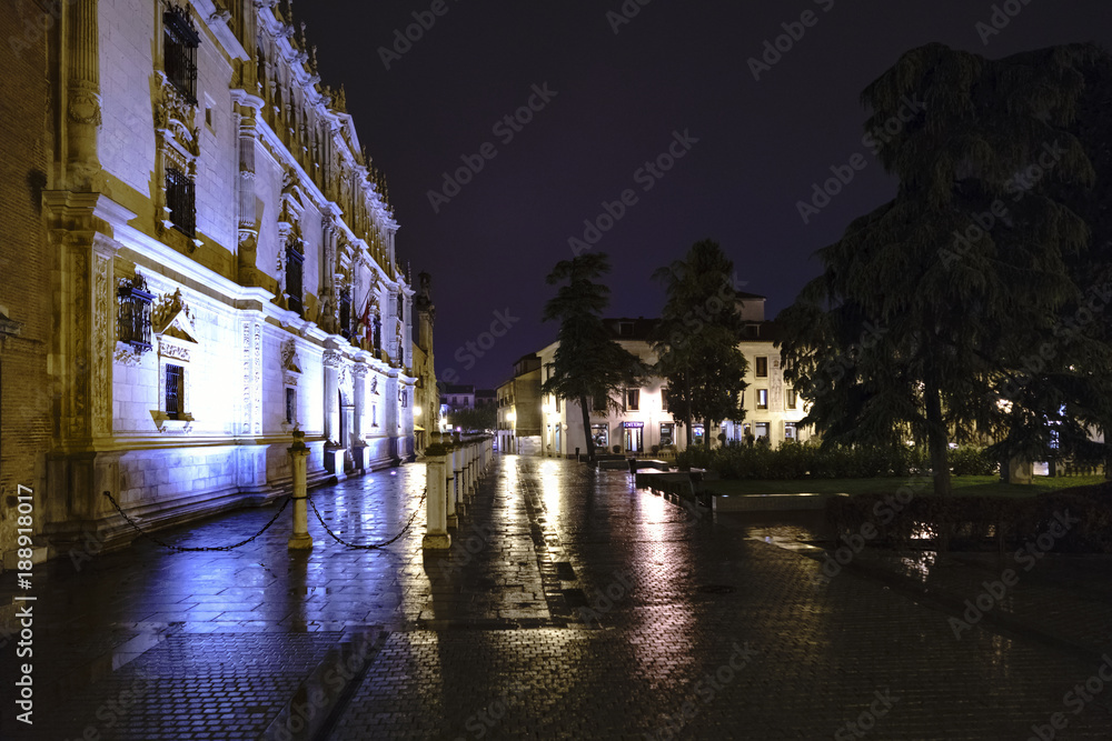 Plaza de San Diego in the center of Alcala de Henares (Spain) with the facade of the Cisneriana University on a cold and rainy night without people and with beautiful light reflections