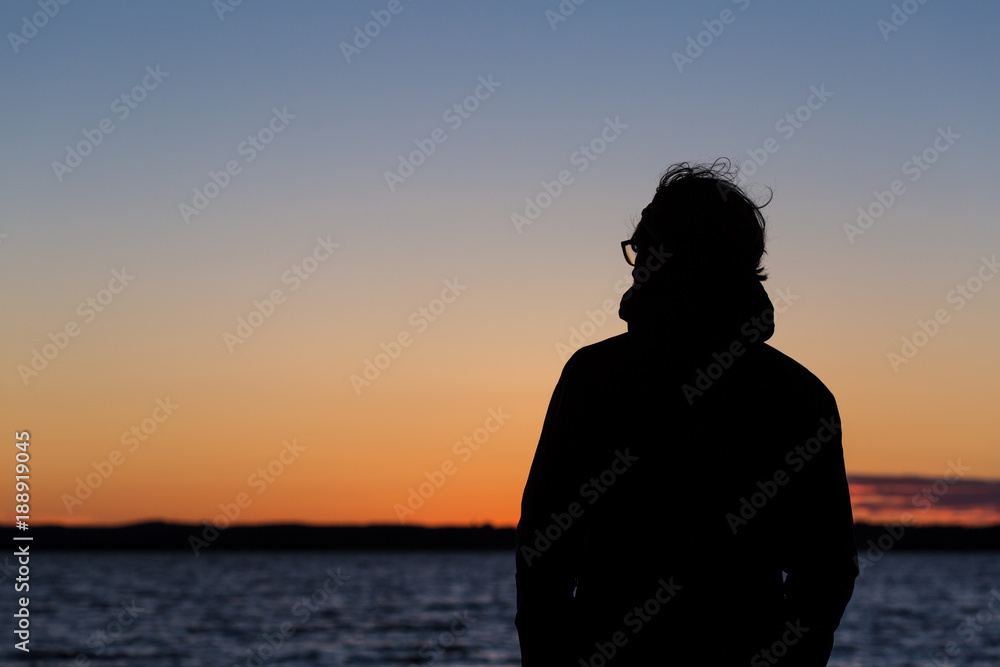 a silhouette of a man in glasses enjoying highly colored sunset at a lake
