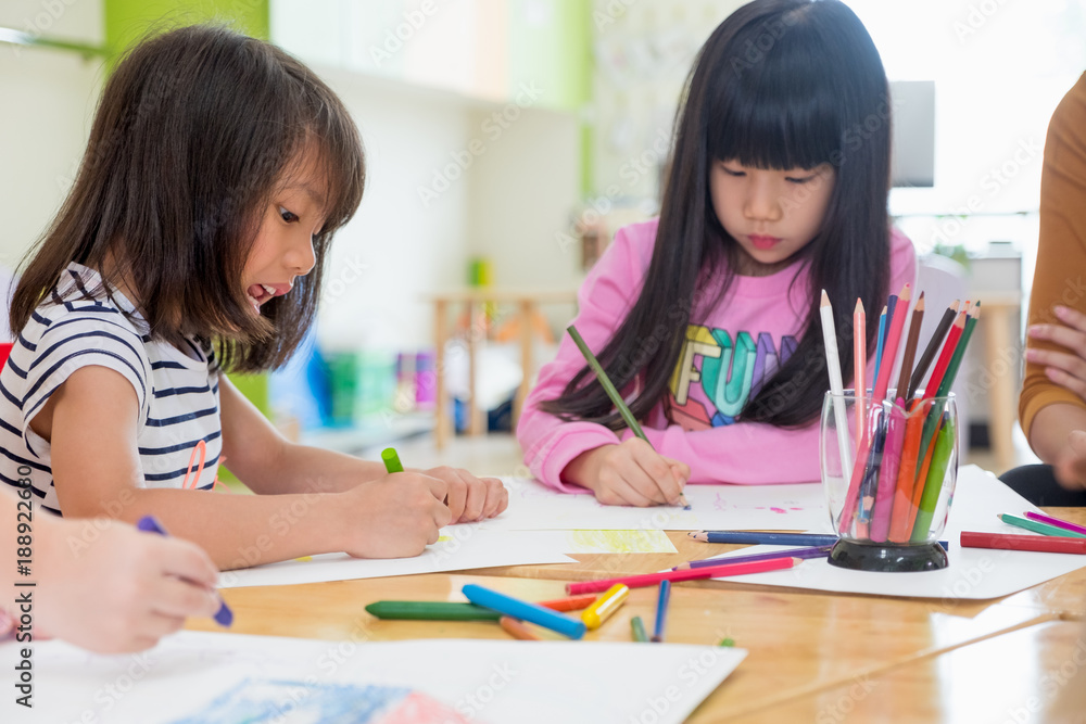 Preschool kids drawing with color pencil on white paper on table in classroom with friends and teacher,Kindergarten education concept. Preschool kids drawing with color pencil on white paper on table in classroom with friends and teacher,Kindergarten education concept.