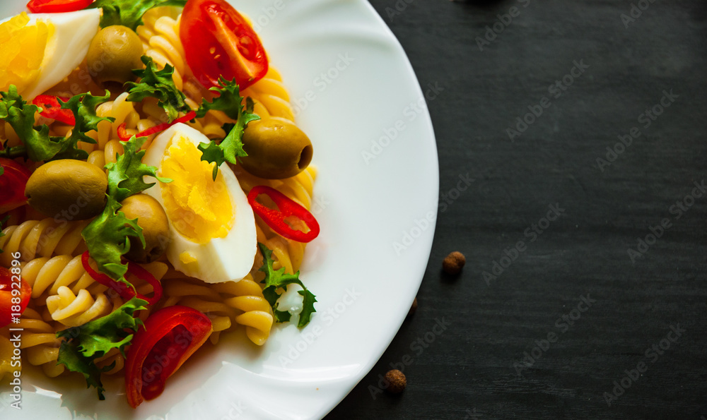 fusilli pasta salad with tomato, eggs and olive in plate on dark wooden background
