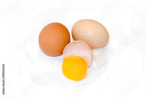 eggs on a white background broken with a yellow yolk and feather