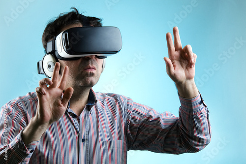 Man using virtual reality glasses and pointing with hands / Adult Man playing game with virtual reality device on a blue background