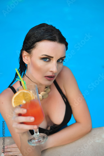 Young woman drink alcohol cocktail with orange on a swimming pool