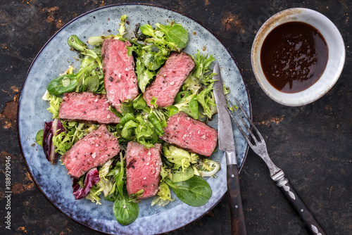 Barbecue wagyu point steak slices with mixed lettuce and hot sauce as top view on a plate