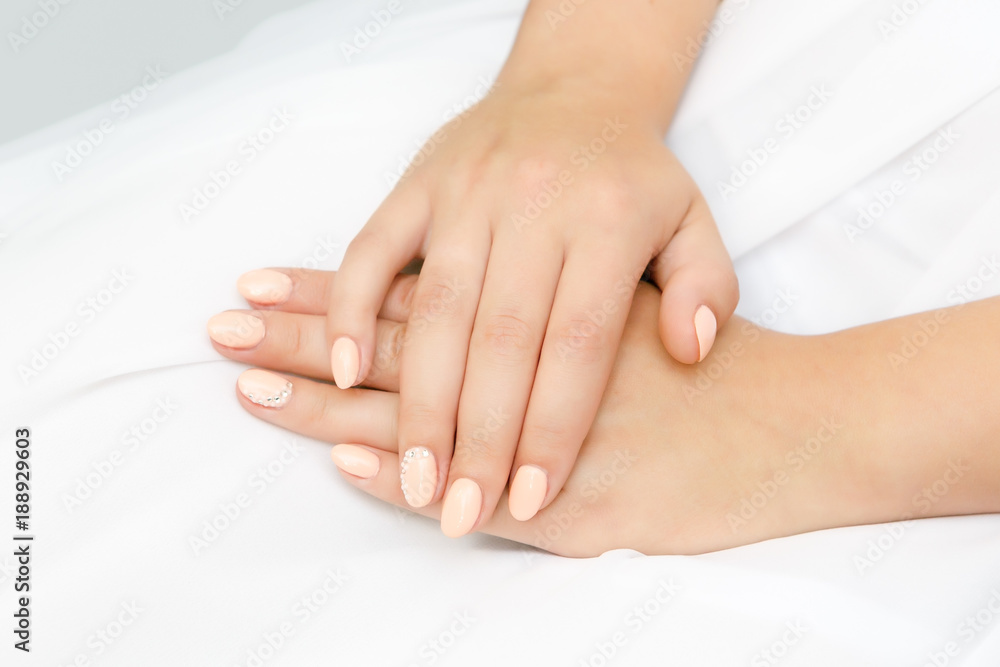 Female hands on a background of white dresses. Glamorous pink manicure with rhinestones.