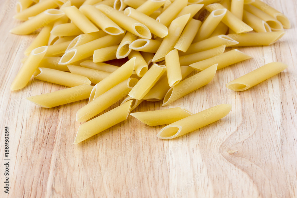 Raw macaroni of hard varieties on a wooden table. A pile of macaroni penne scattered on a close-up table. Raw macaroni of hard varieties on a wooden table. A pile of macaroni penne scattered on a close-up table.