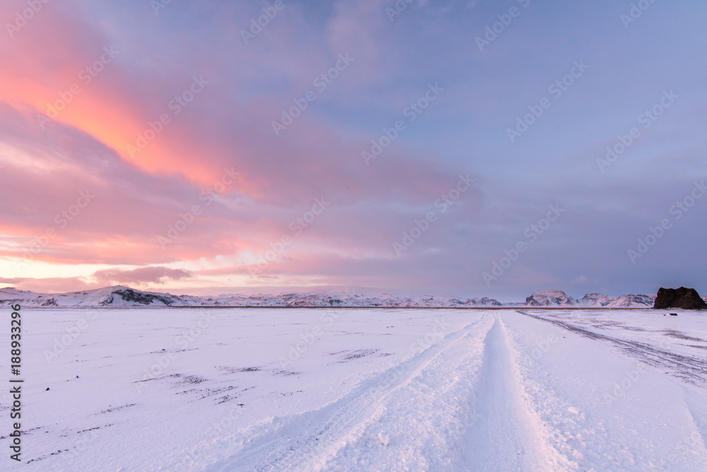The sunsets and reflets off the clouds creating very vivid cloud patterns over tracks in the snow left by an oversize 4x4 vehicle invoking a sense of adventure