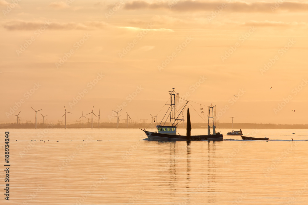Sunset over Dutch sea with fishing ship returning to harbor and windturbines at the horizon