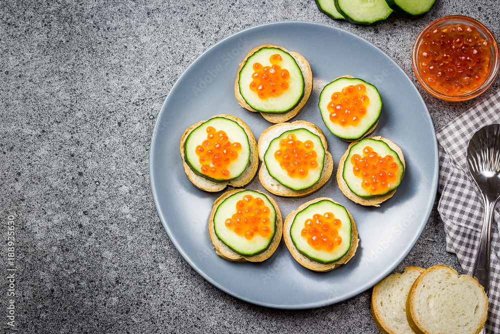 Red caviar cucumber bites on dark concrete background. Top view, space for text.