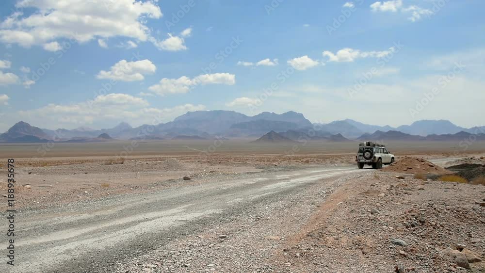 car is moving along a deserted road, raising a lot of dust, chasing a ridge on the horizon, beautiful white clouds car is moving along a deserted road, raising a lot of dust, chasing a ridge on the horizon, beautiful white clouds