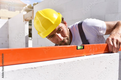 Maurer mit Wasserwaage kontrolliert Rohbau beim Bau eines Einfamilienhauses auf der Baustelle