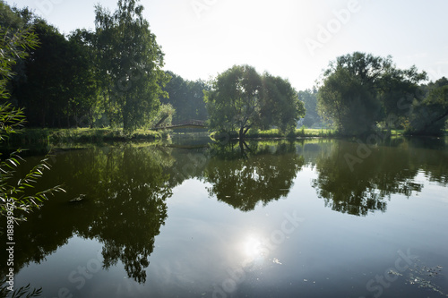 Calm scenery. Barns and forest are reflecting from the water. Foggy landscape.