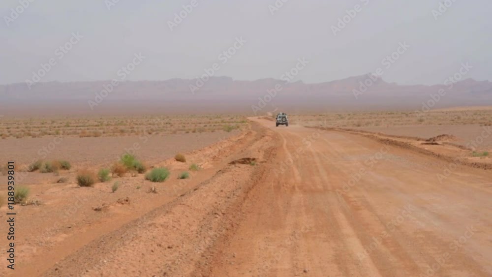 car is moving along a deserted road, raising a lot of dust, chasing a ridge on the horizon, beautiful white clouds car is moving along a deserted road, raising a lot of dust, chasing a ridge on the horizon, beautiful white clouds