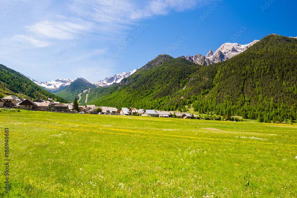 Summer in the Alps, tourist resort, vacation village. Blooming alpine meadow and lush green woodland set amid high altitude mountain range.