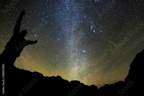 Night sky with Milky Way stars and meteor. Silhouette of a standing man on the twilight pink sky background.
