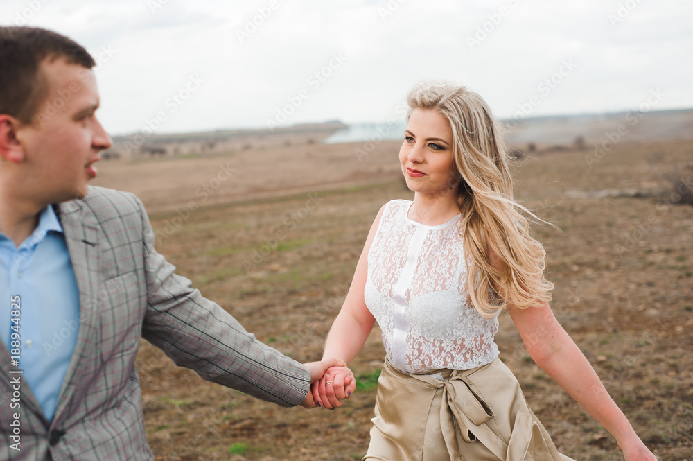 Handsome guy and blonde girl walking on the field, a man leads a woman holding the hand Handsome guy and blonde girl walking on the field, a man leads a woman holding the hand