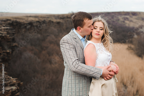 happy young couple hugging on the edge of the mountain, in the background a very beautiful landscape