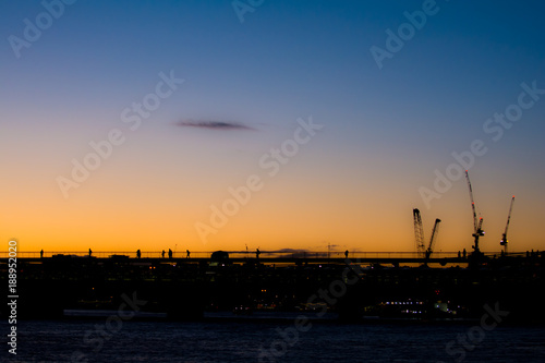 Silhoutted people crossing a city bridge at sunset