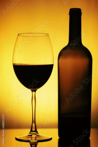 Glass and a Bottle of Wine. Bottle is open, half of it is Wine. Glass and Bottle of wine on a yellow background with a black vignette. Ellegant forms of Bottlr and Glass