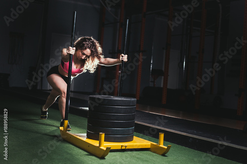 Muscular and strong young female pushing sled on grass turf. Fit woman exercising at cross fit gym. photo