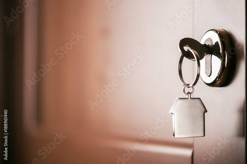Fotografie House key on a house shaped silver keyring in the lock of a entrance  brown door