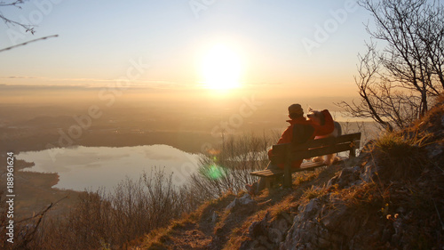 Un ragazzo sulla panchina con il cane osserva il tramonto photo