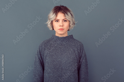 Young woman in a grey sweater studio picture isolated on grey background serious photo