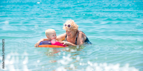  Grandmother and little grandson swim in the sea.The baby in the bouncy multicolored circle.Summer vacation.