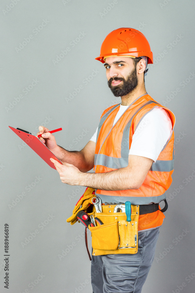 A builder in an orange helmet on a gray background signs something A builder in an orange helmet on a gray background signs something