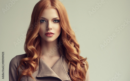 Red head girl with long and shiny wavy hair . Beautiful model woman with curly hairstyle .