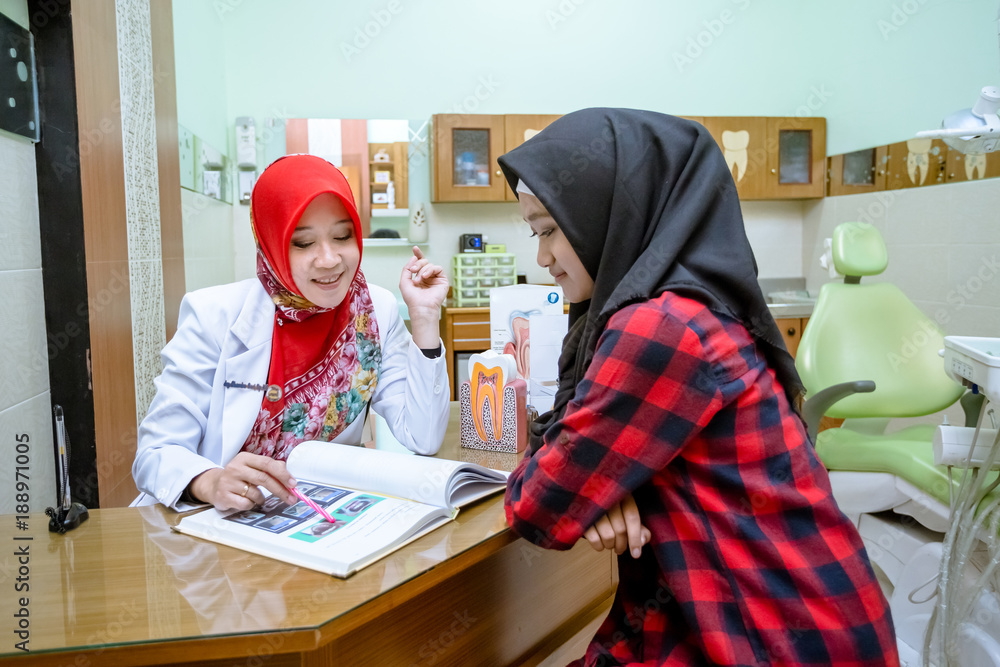 Pretty muslim woman dentist from Indonesia pose in her clinic with her patient