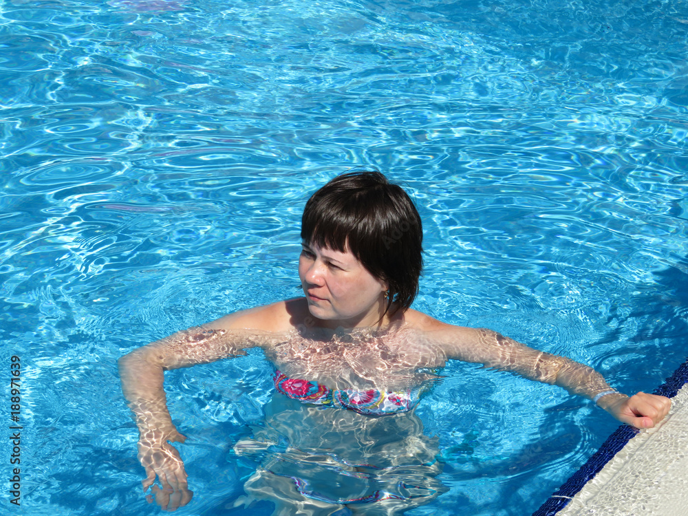 Young woman swims and sunbathes in the pool
