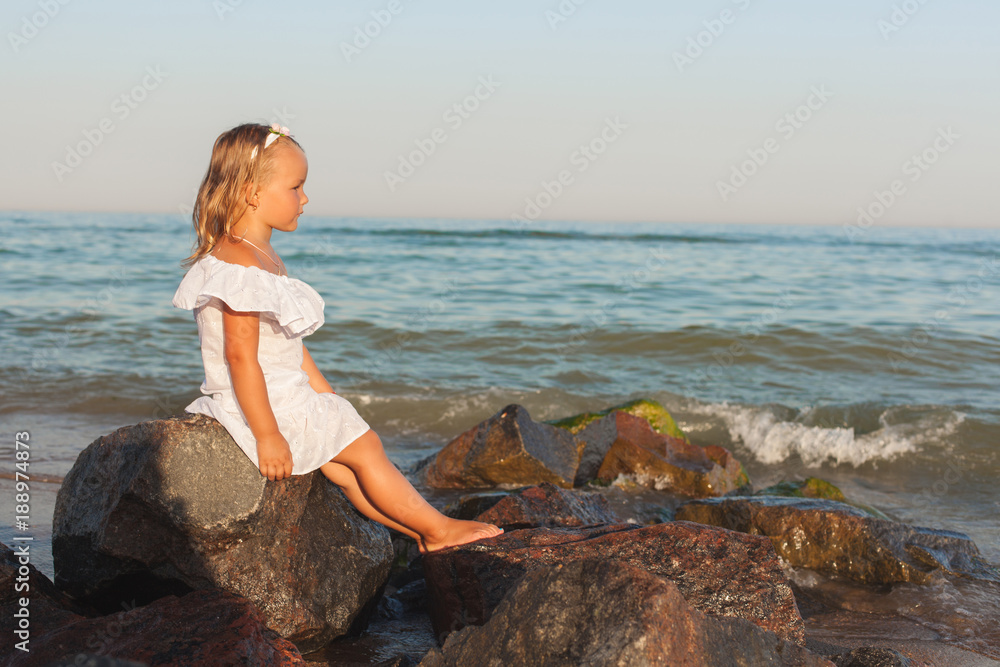 Little girl sitting among the stones by the sea. Little girl sitting among the stones by the sea.