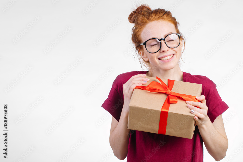 Fototapeta premium Happy dream pretty young redhead woman in glasses holding gift box on white background