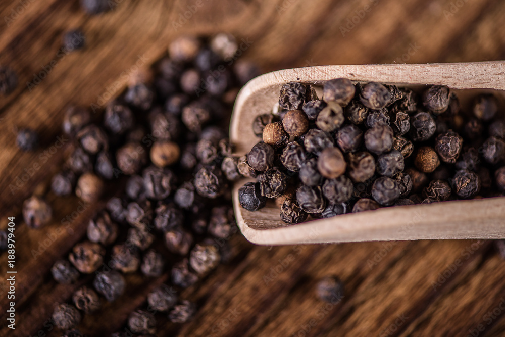 detail close up of whole black peppercorn seasoning spice in wooden spoon on wood table detail close up of whole black peppercorn seasoning spice in wooden spoon on wood table
