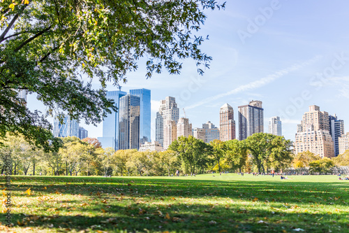 Manhattan NYC Central park Great Lawn in New York City with people walking on green grass meadow in autumn fall season, buildings cityscape skyline