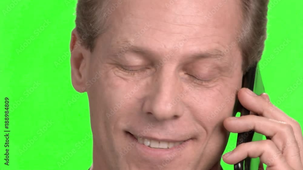 Mature face pleasantly talking on mobile phone. Close up portrait of smiling mature man face talking on cellphone, green hroma background. Mature face pleasantly talking on mobile phone. Close up portrait of smiling mature man face talking on cellphone, green hroma background.