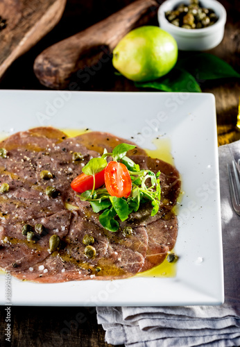 Beef carpaccio on white plate, wooden background. Close up